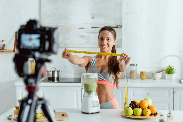 Selektiver Fokus der glücklichen Sportlerin mit Maßband in der Nähe von Früchten und Digitalkamera — Stockfoto