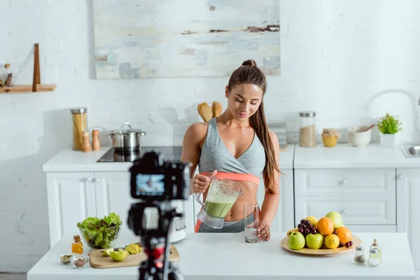 Foyer sélectif de fille heureuse coulant smoothie en verre près de l'appareil photo numérique — Photo de stock