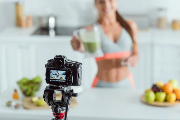 Selective focus of digital camera with happy girl holding smoothie in glass on screen — Stock Photo