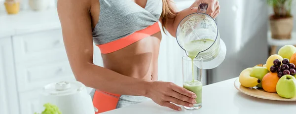 Panoramic shot of girl holding glass while pouring smoothie from blender — Stock Photo