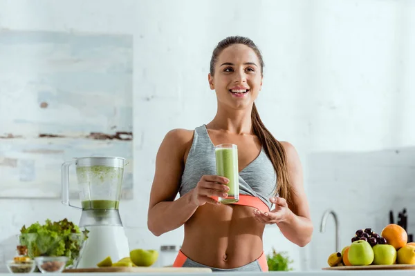 Selective focus of happy girl with sportswear holding glass with tasty smoothie — Stock Photo