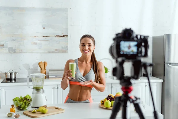 Selective focus of happy girl holding tasty smoothie near digital camera — Stock Photo