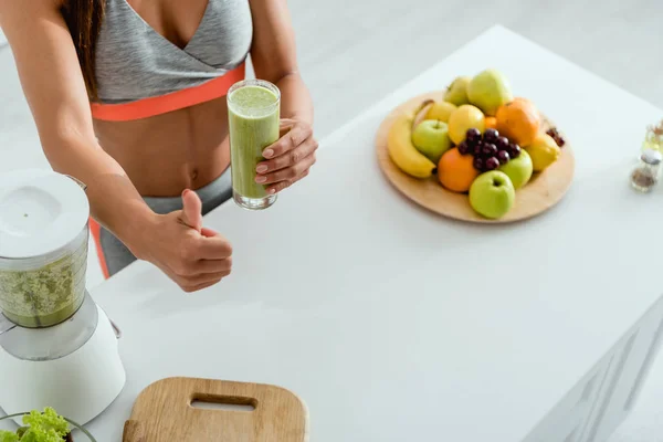 Vista recortada de la mujer mostrando el pulgar hacia arriba mientras sostiene el vidrio con batido - foto de stock