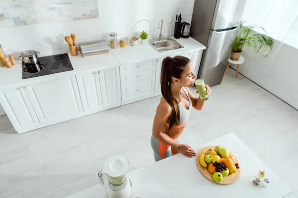 Vista aérea de la mujer bebiendo batido cerca de frutas en la cocina - foto de stock