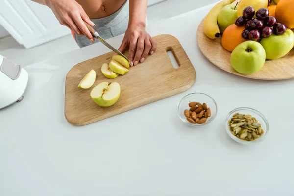 Cropped view of woman cutting apple on cutting board near fruits — Stock Photo