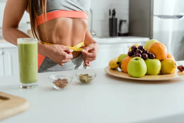 Cropped view of woman measuring waist near fruits — Stock Photo