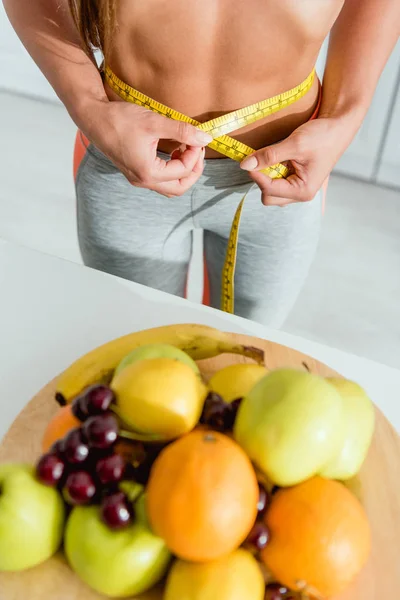 Vue recadrée de la femme tenant du ruban à mesurer tout en mesurant la taille près des fruits — Photo de stock