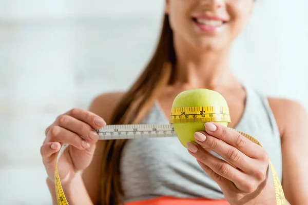 Cropped view of cheerful young woman measuring green apple — Stock Photo