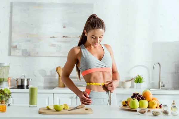 Jovem mulher medindo cintura perto de frutas e bebidas — Fotografia de Stock