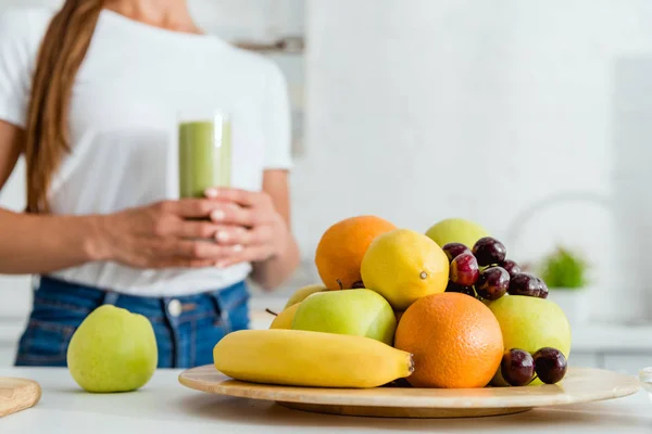 Enfoque selectivo de frutas deliciosas maduras cerca de niña sosteniendo vidrio con batido verde - foto de stock