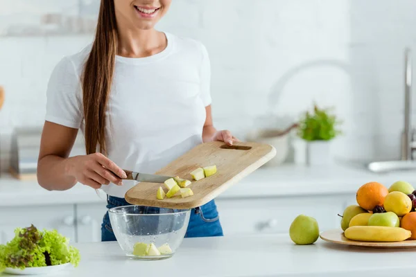 Vista recortada de la joven feliz poniendo manzana verde en rodajas en un tazón - foto de stock