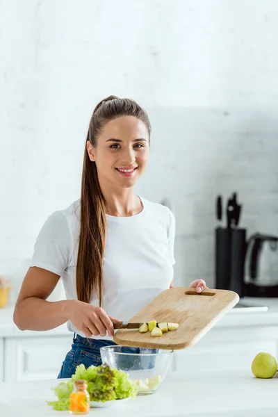 Fröhliche Frau legt geschnittenen grünen Apfel in Schüssel — Stockfoto