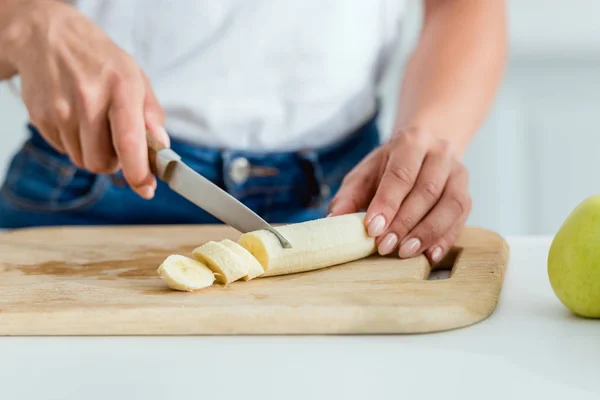 Vista cortada da mulher cortando banana na tábua de corte — Fotografia de Stock
