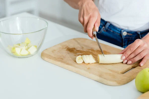 Vue recadrée de la jeune femme coupant banane sur planche à découper — Photo de stock