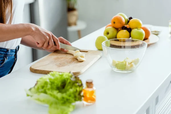 Cropped view of girl cutting tasty banana on chopping board — Stock Photo