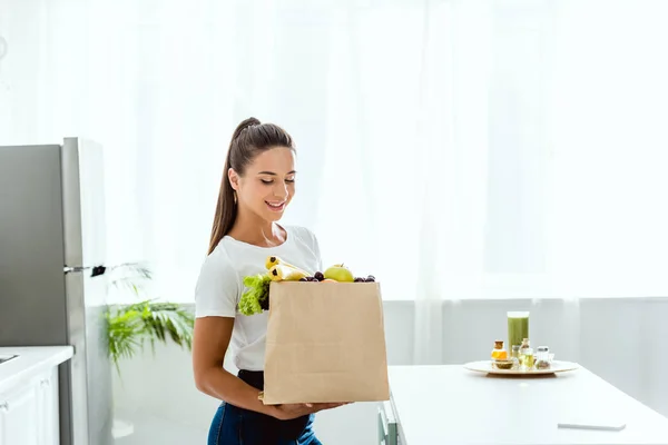 Feliz joven mujer mirando bolsa de papel con frutas - foto de stock