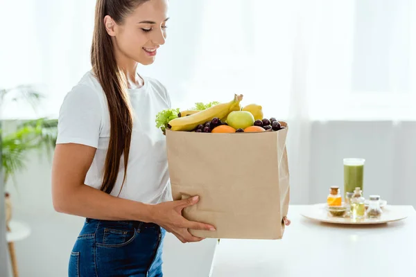 Fröhliche junge Frau blickt auf Papiertüte mit Früchten — Stockfoto