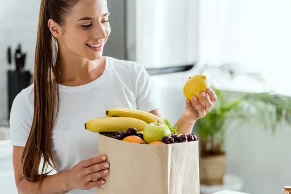 Selective focus of happy girl holding lemon near paper bag with fruits — Stock Photo