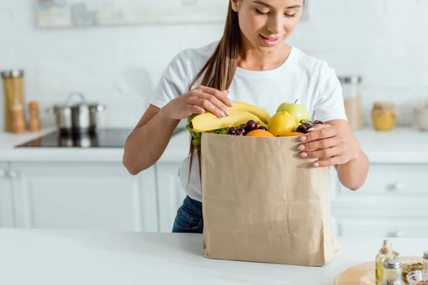 Enfoque selectivo de chica feliz mirando bolsa de papel con frutas - foto de stock