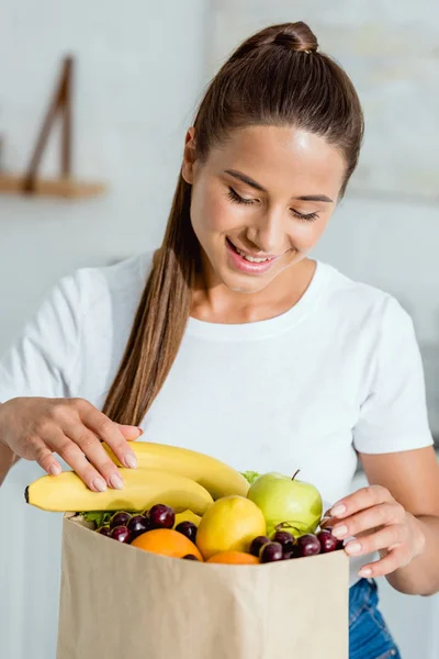 Joyeuse jeune femme regardant les fruits savoureux dans un sac en papier — Photo de stock