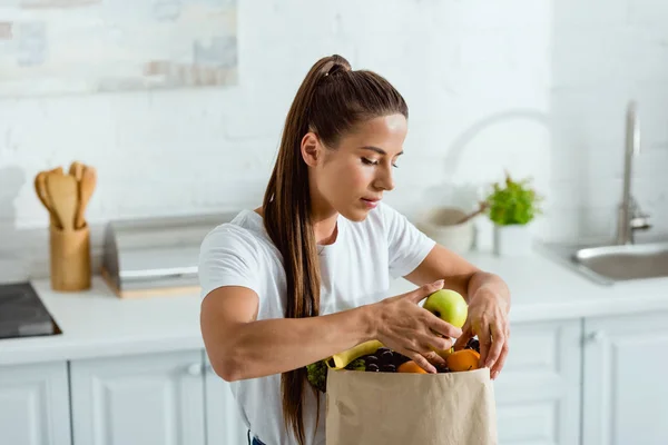 Young woman looking at paper bag and touching fruits — Stock Photo