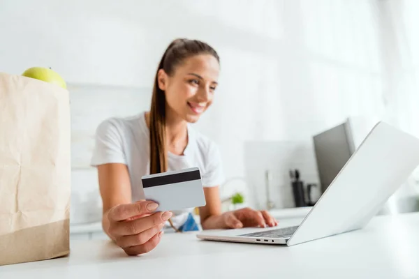 Foco seletivo da menina feliz segurando cartão de crédito e usando laptop — Fotografia de Stock