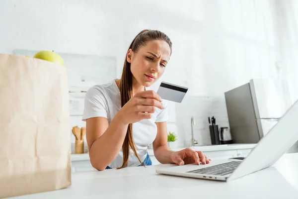 Messa a fuoco selettiva della ragazza guardando la carta di credito e utilizzando il computer portatile — Foto stock