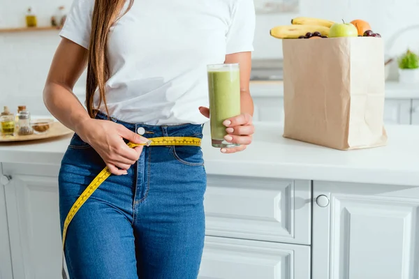 Cropped view of young woman measuring waist near groceries — Stock Photo