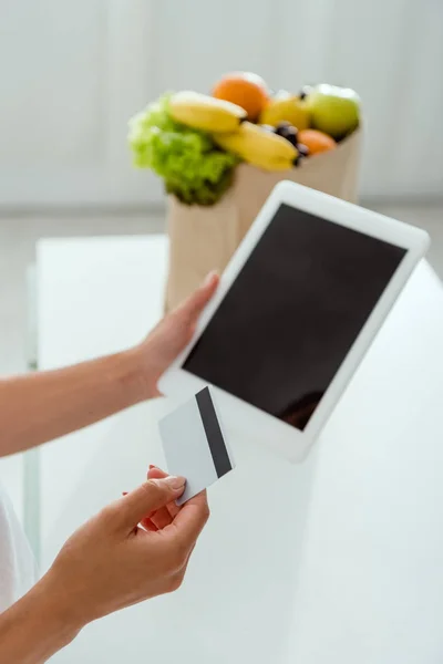 Vista recortada de niña sosteniendo tableta digital con pantalla en blanco y tarjeta de crédito - foto de stock