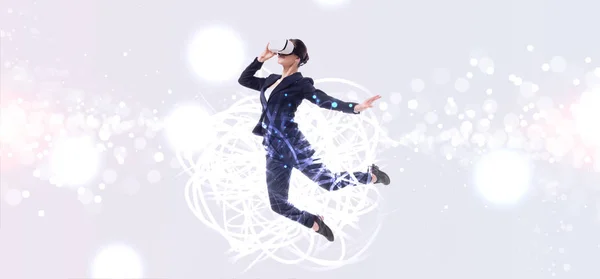 Panoramic shot of businesswoman in virtual reality headset jumping on grey background with abstracts cyberspace illustration — Stock Photo