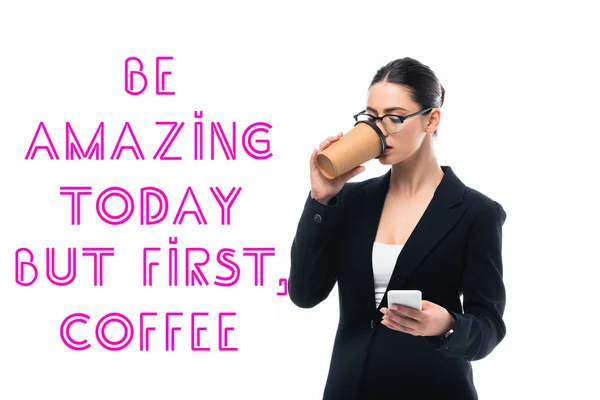 Young businesswoman using smartphone and drinking coffee to go near be amazing but first coffee inscription isolated on white — Stock Photo