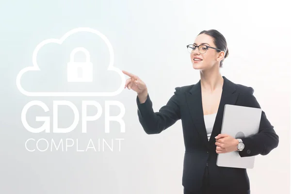 Attractive businesswoman holding laptop and pointing with finger at gdpr compliant safety lock icon on grey background — Stock Photo
