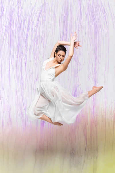 Bailarina atraente em vestido branco vestir-se em fundo cinza com derramamentos coloridos — Fotografia de Stock