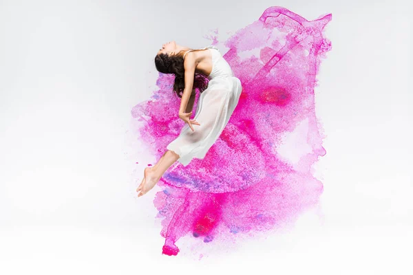 Belle ballerine en robe blanche dansant en peinture violette et rose éclaboussures et déversements sur fond gris — Photo de stock