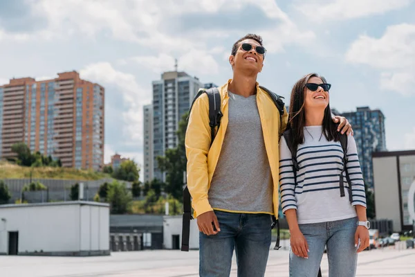 Homme bi-racial mettant la main sur une femme souriante avec sac à dos — Photo de stock