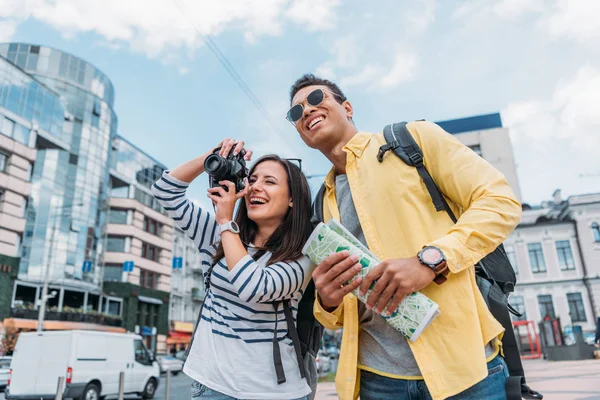 Mulher tirar foto perto de amigo multirracial em óculos de sol segurando mapa — Fotografia de Stock