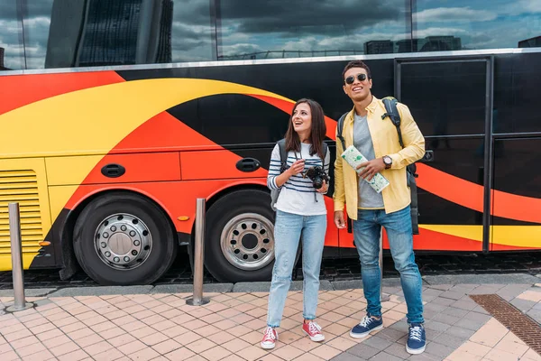 Hombre de raza mixta con mapa y mujer con cámara digital cerca de autobús de viaje - foto de stock