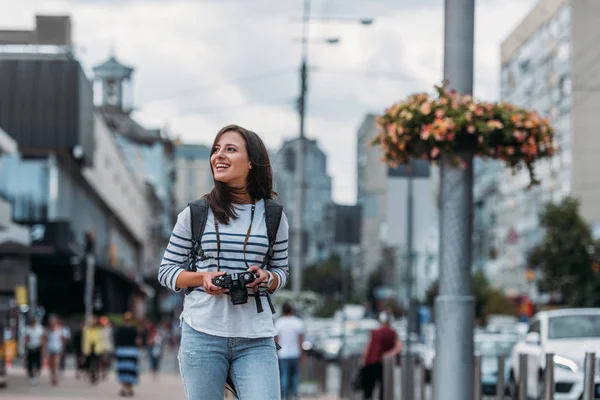 Mujer sonriente con cámara digital mirando hacia otro lado con mochila - foto de stock