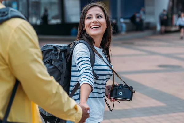 Woman with digital camera and backpack holding hand of friend — Stock Photo