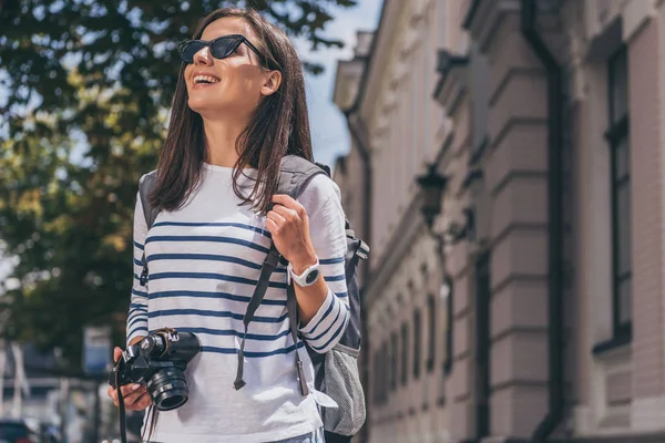 Mulher feliz em óculos de sol com mochila segurando câmera digital — Fotografia de Stock