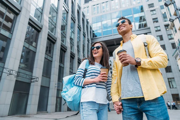 Mujer cogida de la mano de un amigo bi-racial con mochila y taza de papel - foto de stock