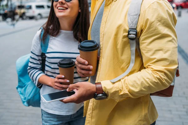 Vista ritagliata della donna con tazza di carta vicino amico bi-razziale con smartphone — Foto stock