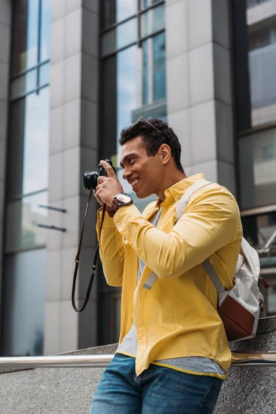 Homem bi-racial com mochila tirando foto na câmera digital — Fotografia de Stock