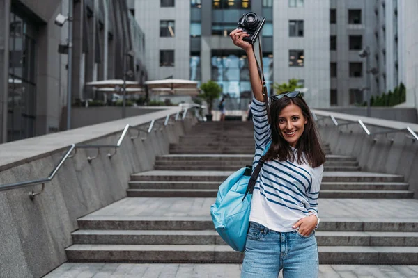Mujer en casual con mochila levantándose de la mano con cámara digital - foto de stock
