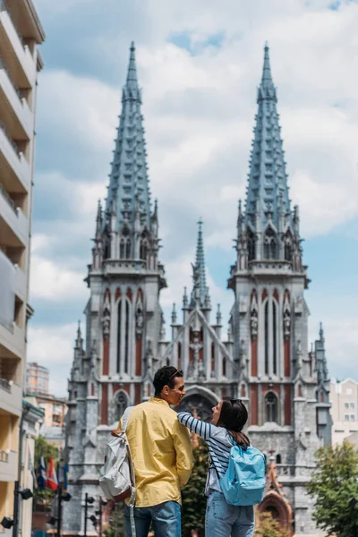 KYIV, UKRAINE - JULY 8, 2019: happy multicultural friends standing near St. Nicholas Roman Catholic Cathedral — Stock Photo
