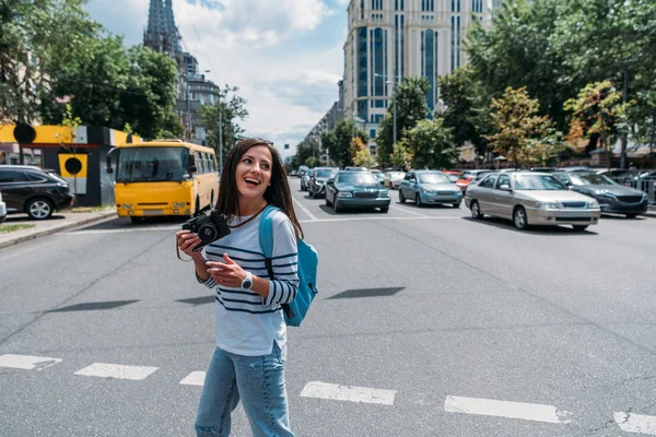 Chica feliz sosteniendo la cámara digital mientras está de pie en la calle con los coches - foto de stock
