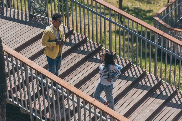 Happy multicultural friends walking with backpacks on stairs — Stock Photo