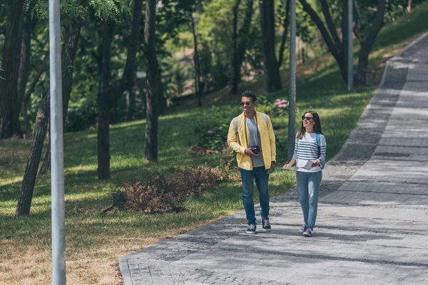 Счастливый мужчина смешанной расы и привлекательная женщина, гуляющие в парке — стоковое фото