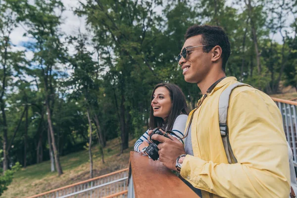 Щасливий чоловік змішаної раси тримає цифрову камеру біля веселої дівчини в парку — стокове фото