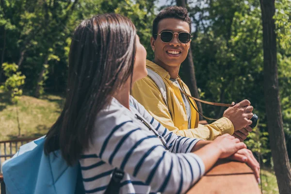 Selective focus of mixed race man in sunglasses looking at girl while holding digital camera — Stock Photo